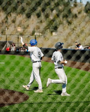 Two baseball players in uniforms run the bases during a sunny outdoor game, with player number 9 raising his hand.