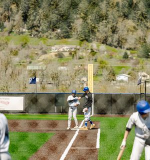 Baseball players at first base during a game with a scenic hillside backdrop on a sunny day.
