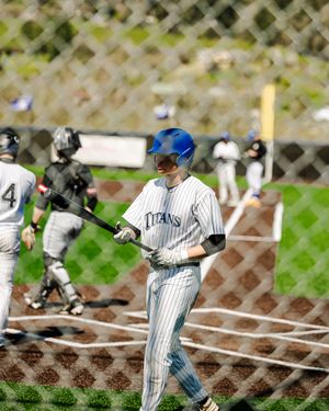 A Titans baseball player in a blue helmet holds a bat near home plate during a game.