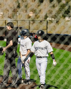 Two Titans baseball players in pinstripe uniforms near dugout with umpire during a sunny game day.