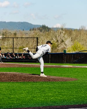 Baseball pitcher in white pinstripe uniform mid-windup on mound with green outfield and hills in background.