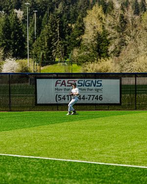 A baseball outfielder stands on a lush green field in front of a FASTSIGNS advertisement banner.