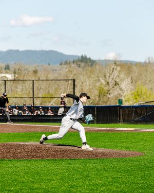 Baseball pitcher in white pinstripe uniform mid-wind-up on mound, green field and mountain backdrop.
