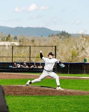 Baseball pitcher in white pinstripe uniform releasing pitch from mound at outdoor ballpark with mountain backdrop.