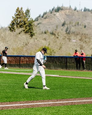 Baseball player in pinstripe uniform walks along the field during a spring game with hills in the background.