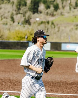 Baseball player in pinstripe uniform jogging on field wearing black cap and glove on sunny day.