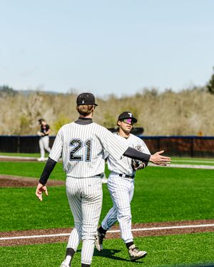 Two baseball players in white pinstripe uniforms exchange a high five on the field, player 21 visible from behind.