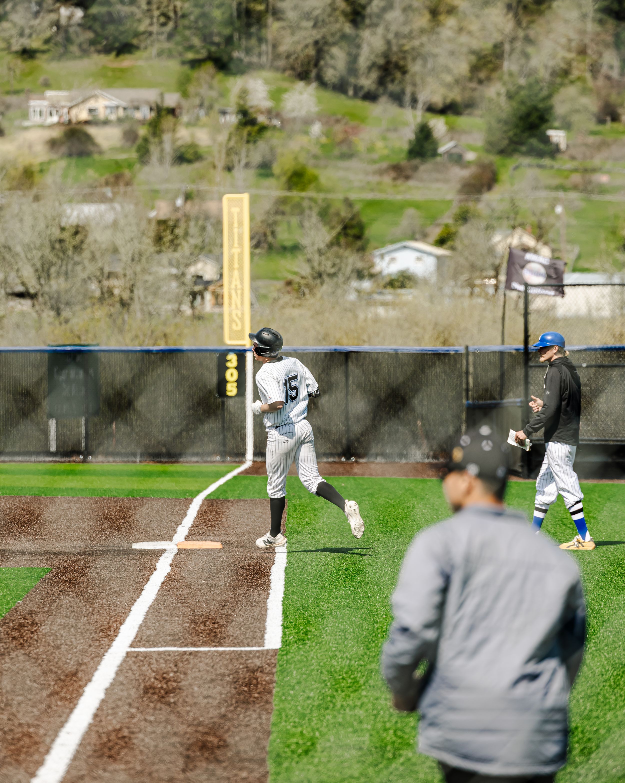 Baseball player in white uniform running bases during a game on a green field with hills in the background.