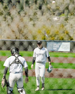 Two Titans baseball players in white pinstripe uniforms walk on a green field during a sunny outdoor game.