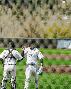 Two Titans baseball players in pinstripe uniforms on a green field, one wearing catcher gear, during a spring game.