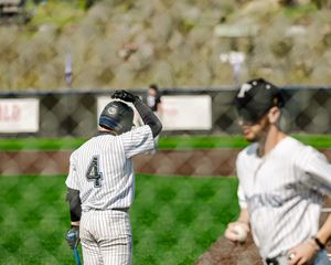 Baseball player number 4 raises glove at home plate as teammate approaches during sunny outdoor game.