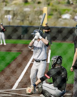Baseball batter in Titans pinstripe uniform stands ready at home plate with catcher crouching behind during a game.