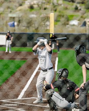 Baseball batter in pinstripe uniform stands ready at home plate with catcher and umpire during a spring game.