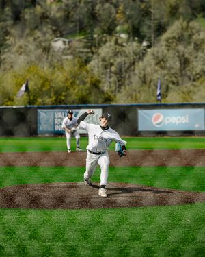Titans baseball pitcher mid-throw on mound during game with Pepsi ad and green hillside in background.