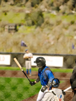 Baseball batter in blue jersey and helmet prepares to swing at home plate during an outdoor game.