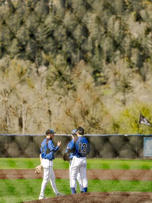 Three baseball players in blue uniforms having a mound meeting on a green field with trees in the background.