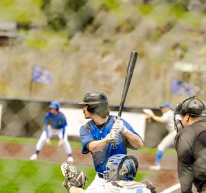 Baseball batter in blue uniform at plate, catcher crouching, umpire standing by, players visible in background on field.