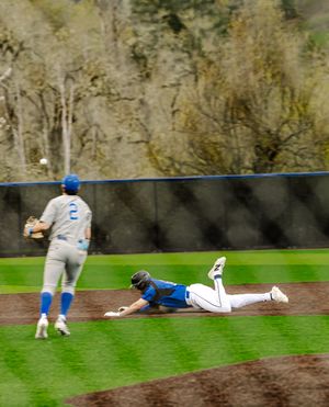 Baseball player slides on field while teammate in number 2 jersey watches during a game.