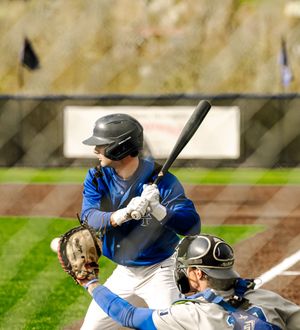 Baseball batter in blue jersey swings at pitch with catcher crouching behind home plate during a game.
