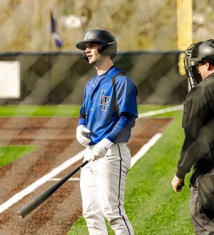 Baseball batter in blue uniform holds bat at home plate while umpire stands nearby during a game.
