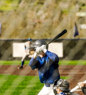 Baseball batter in blue jersey swings at pitch with catcher behind home plate and outfielder visible in background.