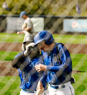 Two baseball players in blue helmets and uniforms celebrate on the field during a game.