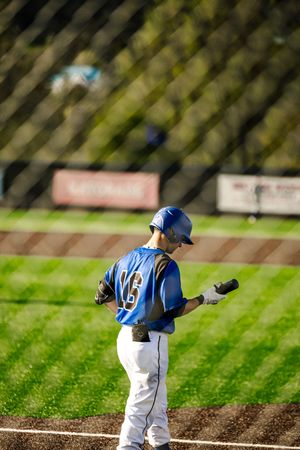 Baseball player #16 in blue helmet and uniform walks near home plate holding batting gloves during a game.