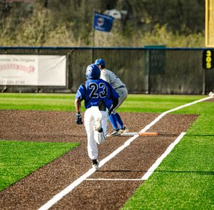 Baseball player #23 in blue uniform rounds first base during a game on a bright green turf field.