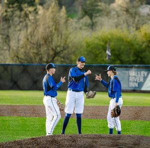 Three baseball players in blue uniforms huddle on the pitcher's mound during a game near Valley River Inn.