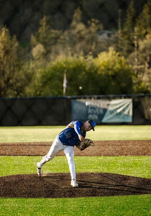 A baseball pitcher in a blue uniform delivers a pitch from the mound during a sunny outdoor game.