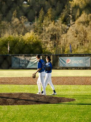 Two baseball players in blue uniforms walk on the pitcher's mound during a game with a Pepsi banner in background.