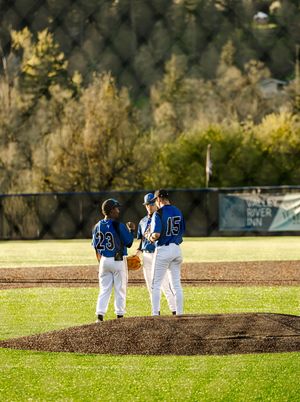 Three baseball players in blue uniforms huddle on the pitcher's mound during a game.