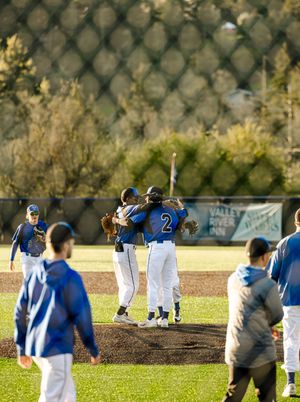 Baseball players in blue uniforms celebrate on the field, hugging near the pitcher's mound during a sunny game.