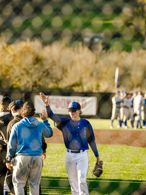 Baseball player in blue uniform high-fiving teammate near dugout during sunny outdoor game.