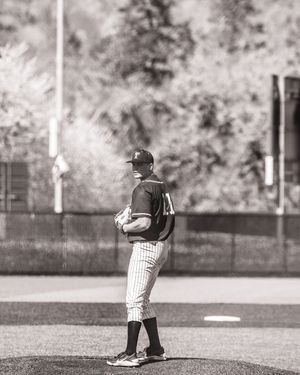Black and white photo of baseball pitcher standing on mound in pinstripe uniform ready to deliver pitch.