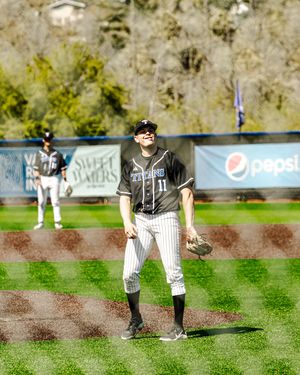 Baseball player #11 in black Titans jersey stands on outfield grass during a sunny game.