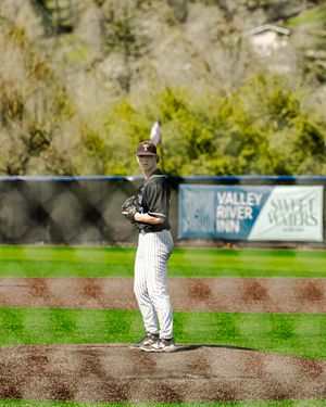 A baseball pitcher stands on the mound at Valley River Inn field, wearing a black and white pinstripe uniform.
