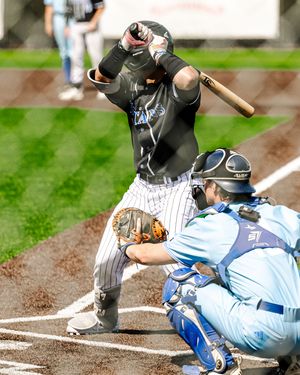 Baseball batter in pinstripe uniform swinging while catcher in blue gear crouches at home plate.
