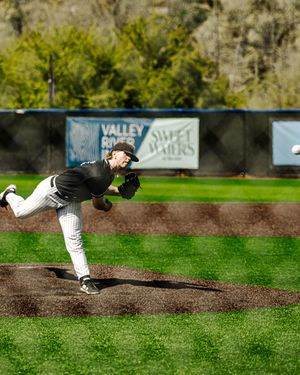 Baseball pitcher in black uniform delivers pitch on mound with Valley River Inn sign behind.