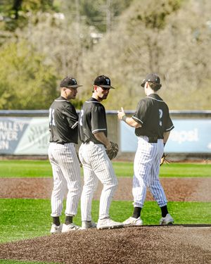 Three baseball players in black pinstripe uniforms huddle on pitchers mound during game.