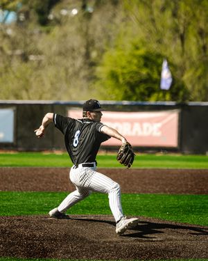 Baseball pitcher in black pinstripe uniform winding up to throw on the mound during a sunny outdoor game.
