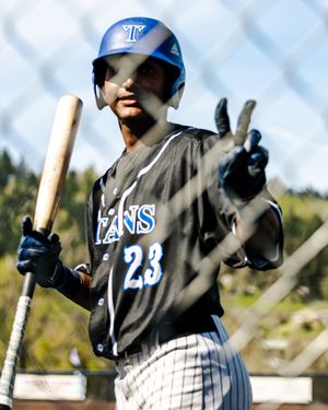Baseball player #23 in Titans uniform holds bat and flashes peace sign near dugout fence.