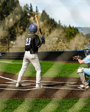 Baseball batter number 23 stands at home plate ready to swing as catcher crouches behind on a sunny day.