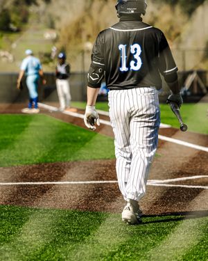 Baseball player wearing jersey number 13 walks toward home plate carrying a bat during a sunny outdoor game.