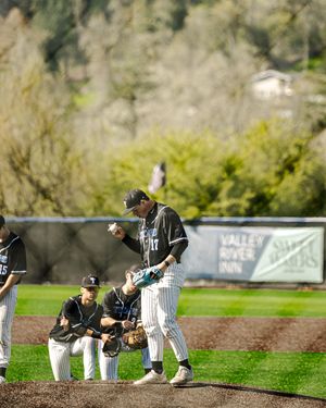 Baseball players in black pinstripe uniforms celebrate on field near Valley River Inn banner.