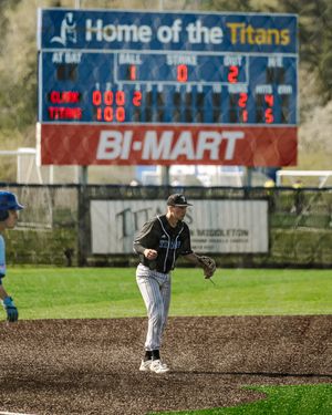 Baseball player in Titans uniform fielding on diamond, scoreboard reads Home of the Titans, Bi-Mart ad visible.