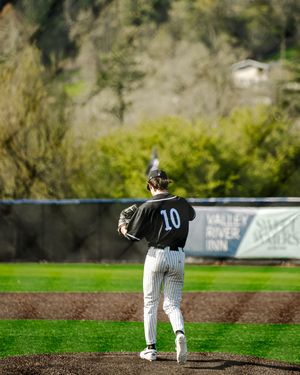 Baseball pitcher wearing number 10 black uniform winds up to throw on pitching mound at outdoor ballpark.