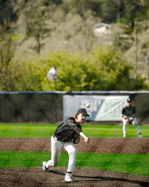 Baseball pitcher in black uniform delivers a pitch from the mound during a game.