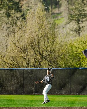 Outfielder in black uniform prepares to catch a fly ball against a backdrop of spring blossoming trees.