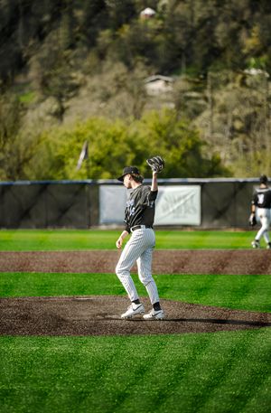 A baseball pitcher in a black uniform catches a ball on the mound during an outdoor game.